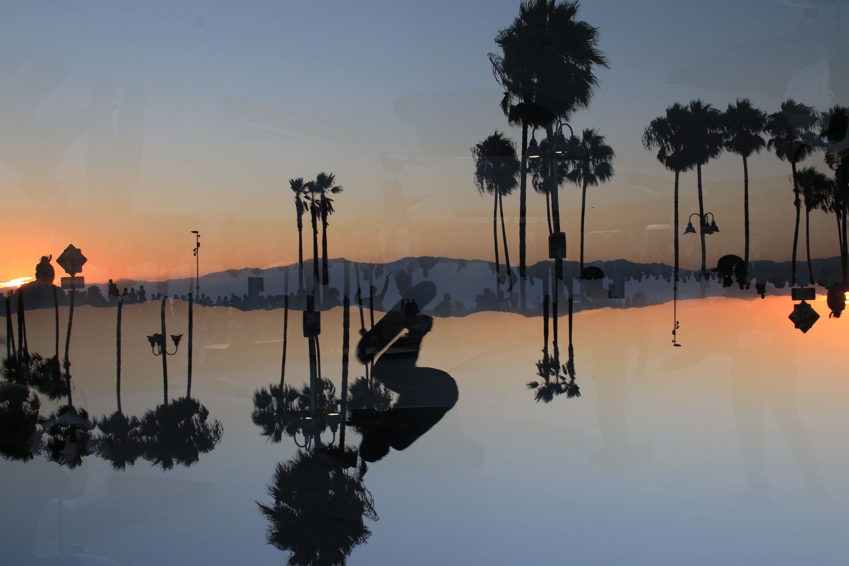 Beach walkers and palm trees mirrored against a sunset